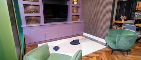 A modern living room with a large flat-screen TV, built-in shelving, and a herringbone-patterned wooden floor.