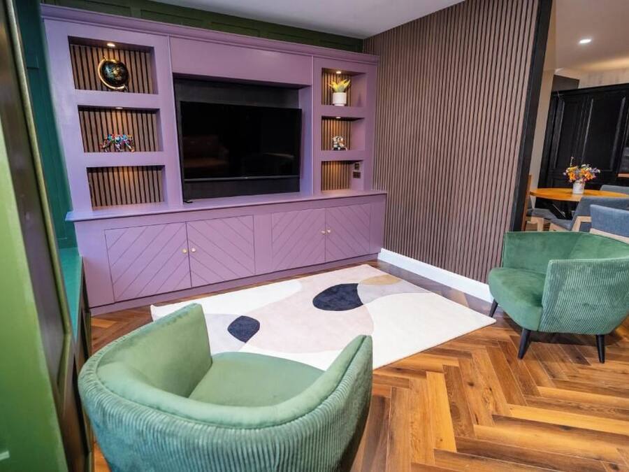 A modern living room with a large flat-screen TV, built-in shelving, and a herringbone-patterned wooden floor.