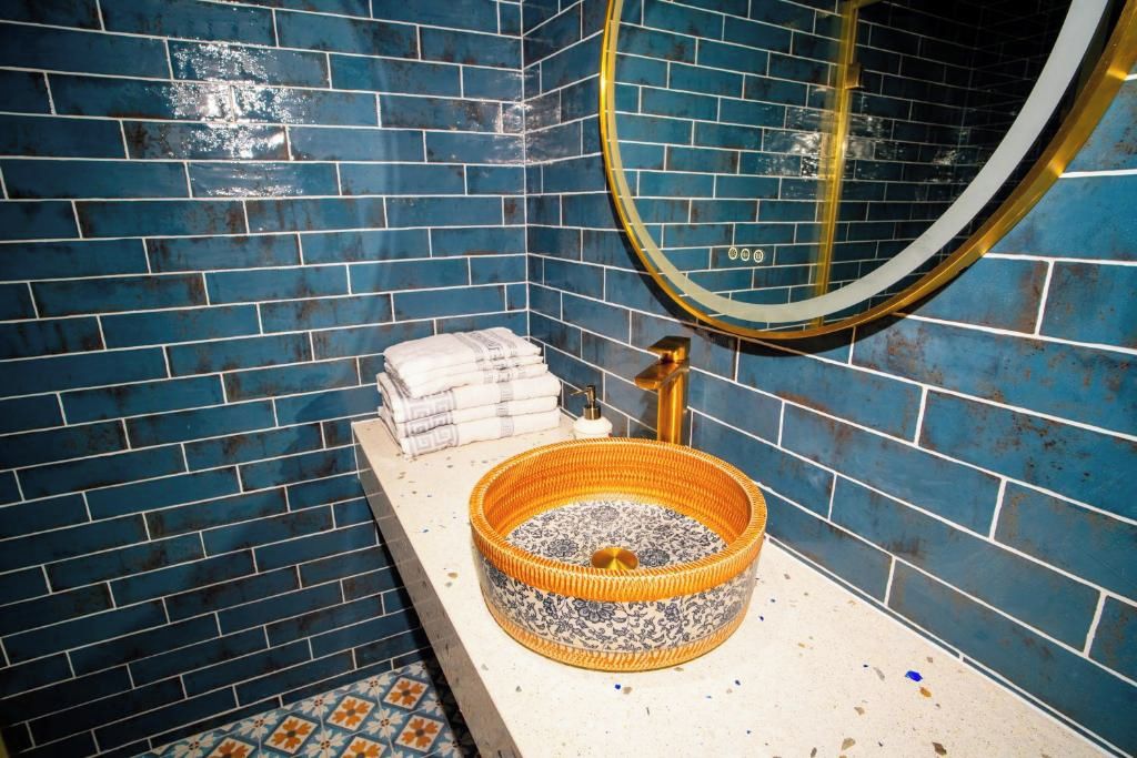 A bathroom with blue tiled walls, a round mirror, a sink with a decorative basin, and a towel rack.