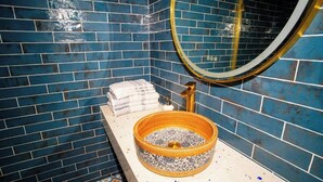 A bathroom with blue tiled walls, a round mirror, a sink with a decorative basin, and a towel rack. - Woolen house  (MO)