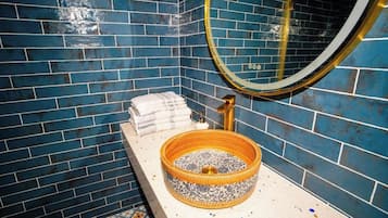 A bathroom with blue tiled walls, a round mirror, a sink with a decorative basin, and a towel rack.
