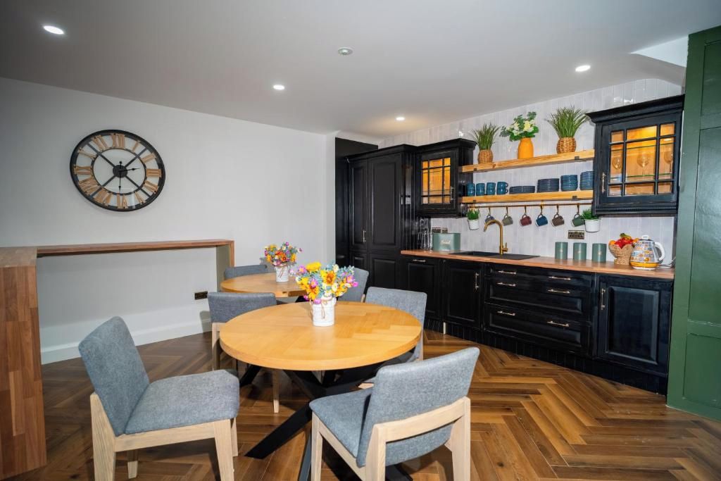 A modern kitchen with black cabinets, a wooden dining table, and a clock on the wall.