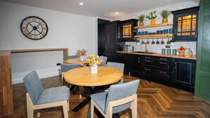 A modern kitchen with black cabinets, a wooden dining table, and a clock on the wall. - Woolen house  (MO)