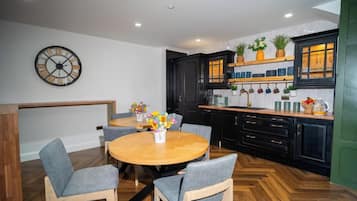 A modern kitchen with black cabinets, a wooden dining table, and a clock on the wall.