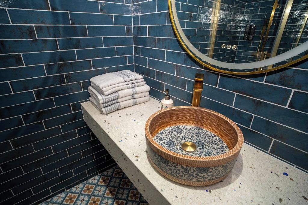 A bathroom with a blue-tiled wall, a round sink with a decorative basin, and a stack of towels on a shelf.