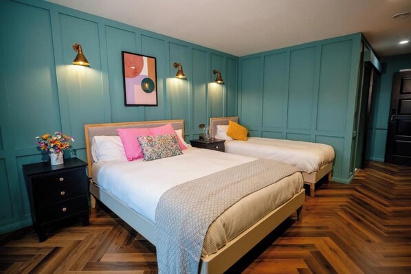 A room with two beds, a nightstand, and wall-mounted lamps.