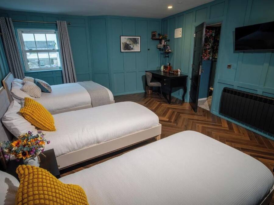 Una habitación con dos camas, un escritorio, una silla, un televisor y un ventanal con cortinas.