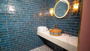 A bathroom with blue tiled walls, a white countertop, a round mirror, and a patterned basin. - Woolen house  (MO)