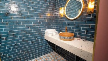 A bathroom with blue tiled walls, a white countertop, a round mirror, and a patterned basin.