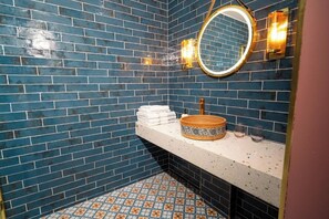 A bathroom with blue tiled walls, a white countertop, a round mirror, and a patterned basin. - Woolen house  (MO)