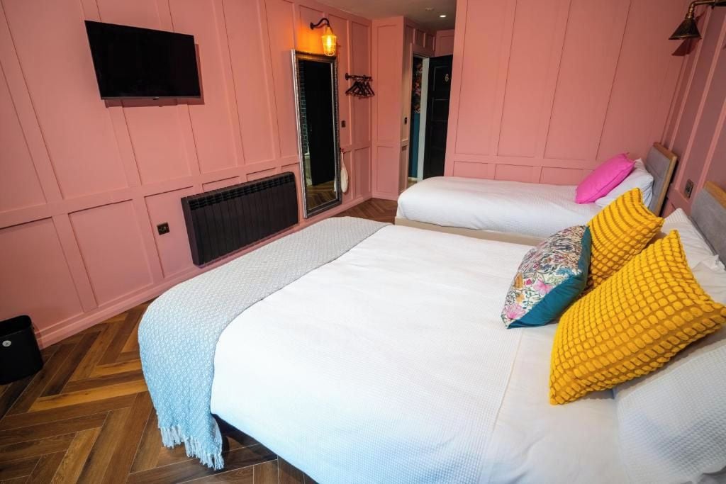 A hotel room with two beds, a television, a mirror, and a door.