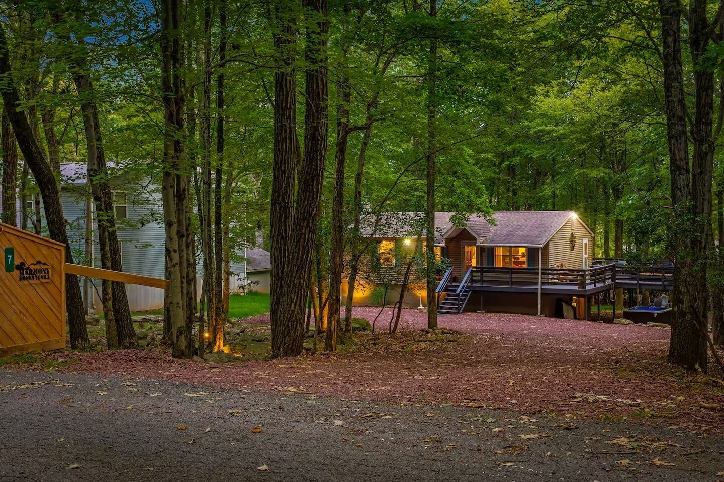 A cabin with a deck and a staircase leading to a covered area, surrounded by tall trees.