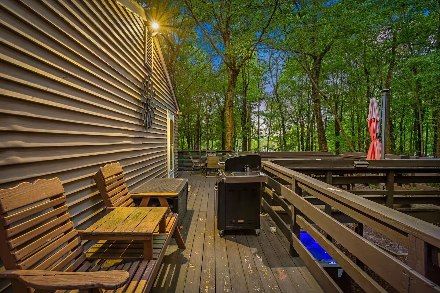 A wooden deck with a grill, seating, and a view of a forest.