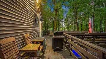 A wooden deck with a grill, seating, and a view of a forest.