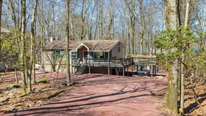 A cabin with a porch and a covered deck area, surrounded by trees. - Honky Tonk Karaoke! Hot Tub - Sauna - 5 min wlk 2 lake (Lake Harmony)