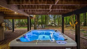 A hot tub under a wooden pergola in a wooded area with outdoor seating.