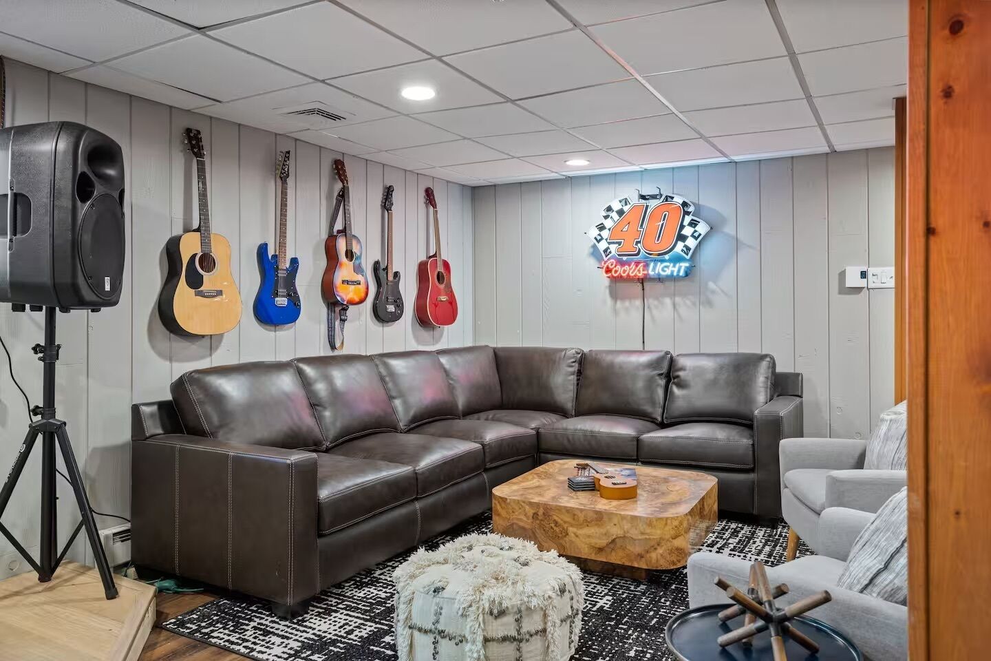 A room with a brown leather sectional sofa, a coffee table, and a wall-mounted guitar display.