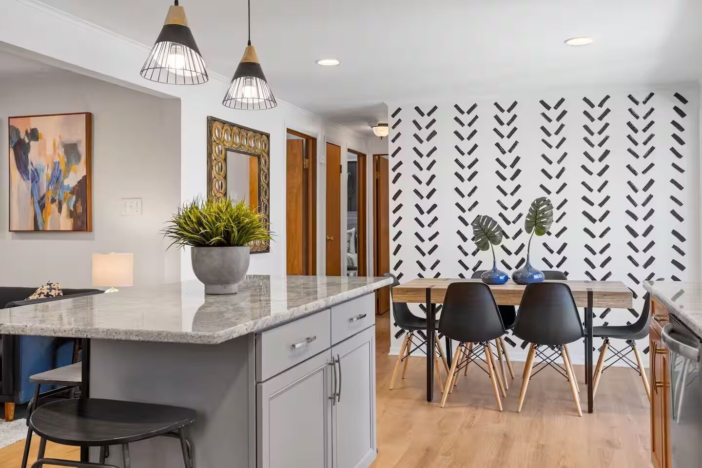 A modern kitchen with a central island, pendant lighting, and a dining area with a patterned wall.