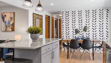 A modern kitchen with a central island, pendant lighting, and a dining area with a patterned wall.