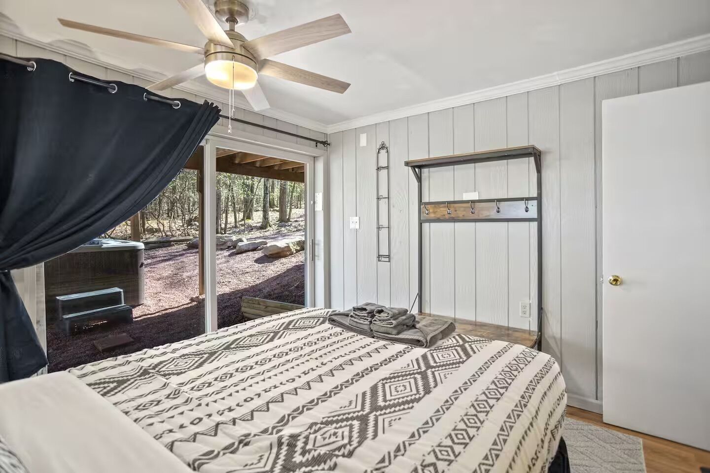 A bedroom with a bed, a ceiling fan, a sliding door to a deck, and a small table with towels.