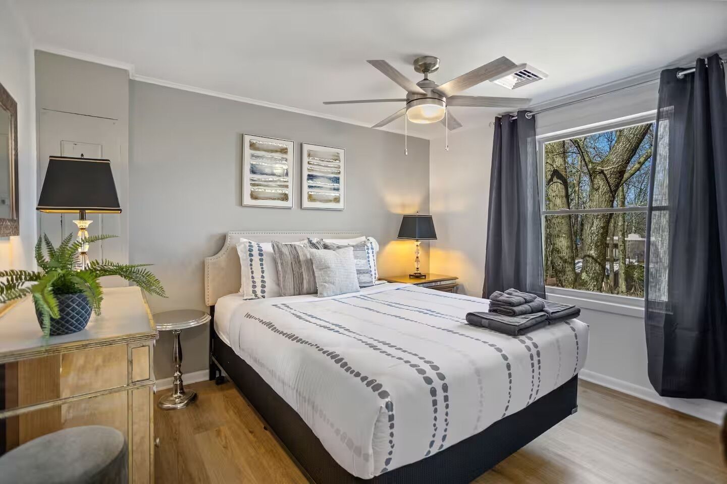 A bedroom with a bed, two bedside tables, a ceiling fan, and a window with curtains.