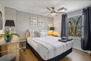 Un dormitorio con una cama, dos mesitas de noche, un ventilador de techo y una ventana con cortinas.