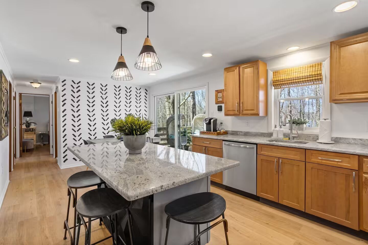 A modern kitchen with a central island, bar stools, wooden cabinets, and pendant lighting.