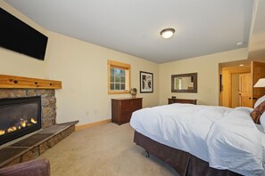 A bedroom with a stone fireplace, a bed, a dresser, a mirror, and a television mounted on the wall. - Yocum Ridge Condo 204 at South Grand Lodge | Best Mt. Hood View (Government Camp)