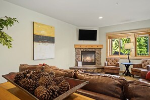 A living room with a stone fireplace, leather sofas, and a television mounted on the wall. - Yocum Ridge Condo 204 at South Grand Lodge | Best Mt. Hood View (Government Camp)