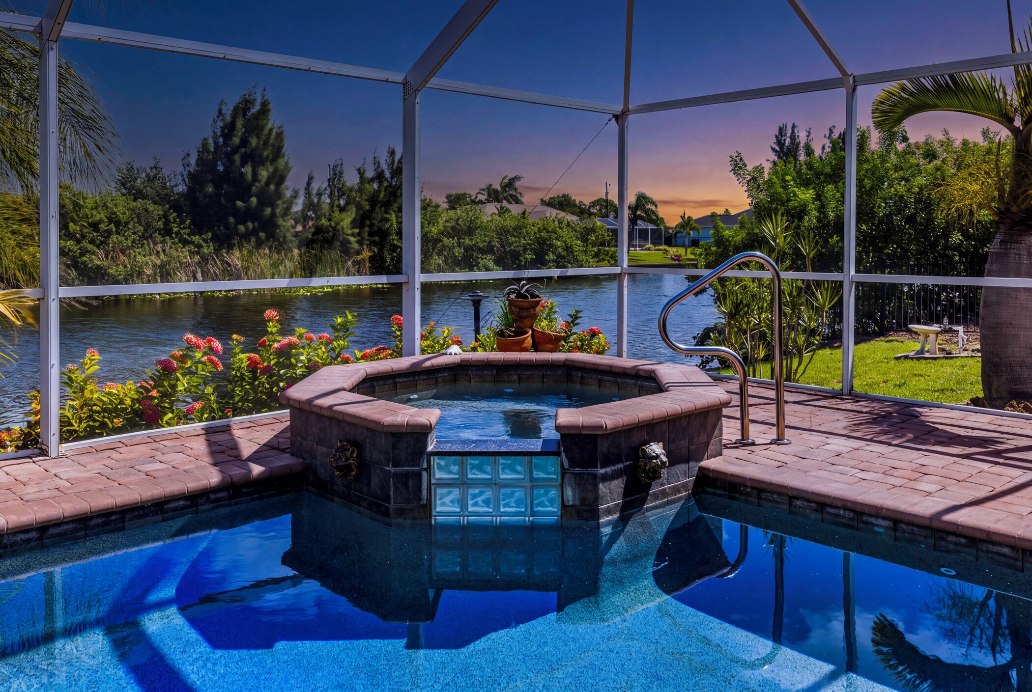 Een zwembad met een jacuzzi, omringd door een overdekt terras met uitzicht op een meer en groen.