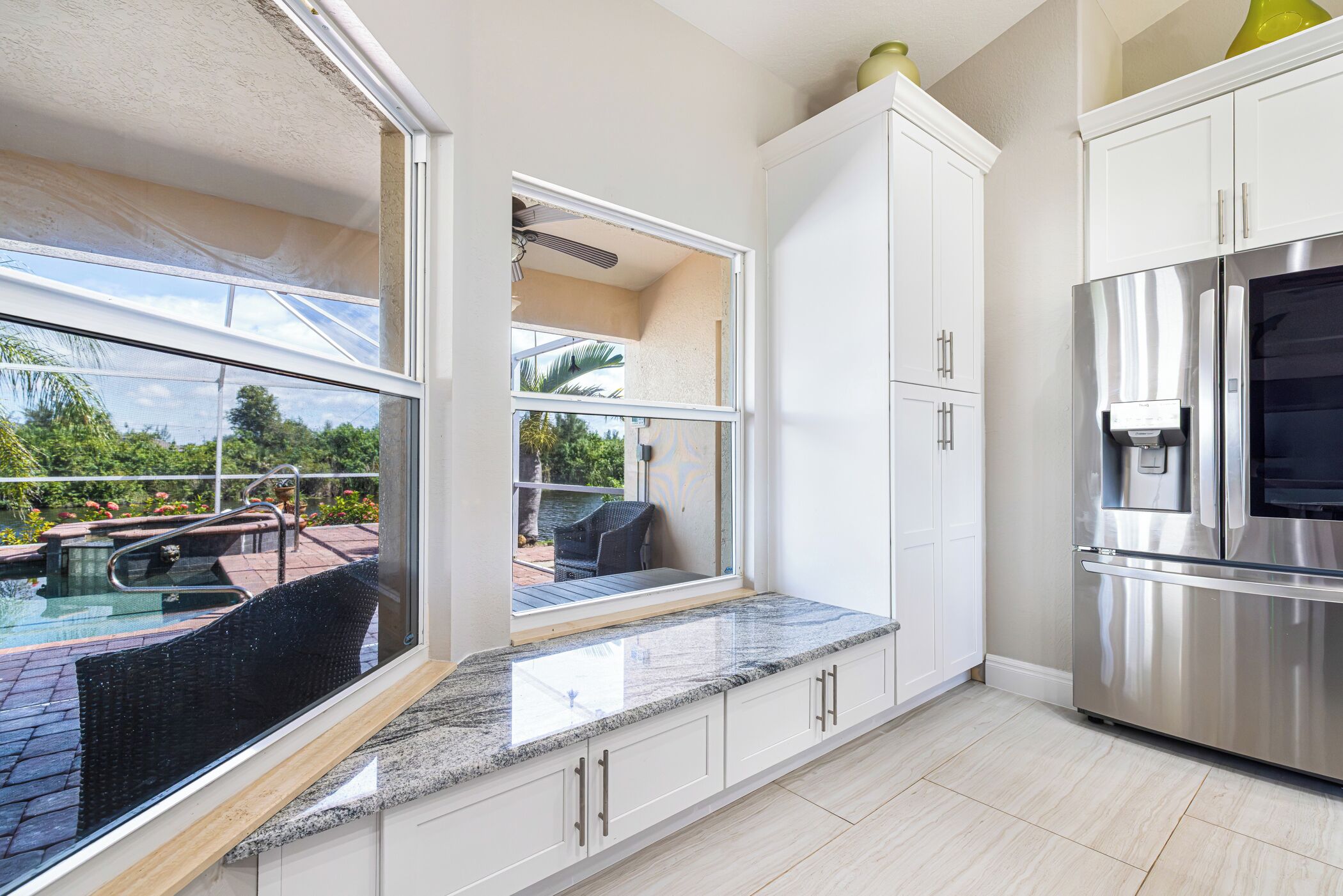 A modern kitchen with a built-in refrigerator, a water dispenser, and a large window overlooking a pool area.