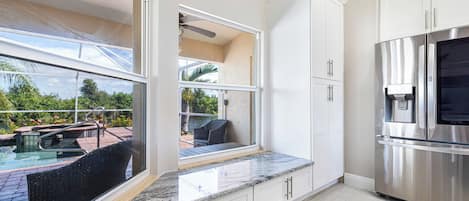 A modern kitchen with a built-in refrigerator, a water dispenser, and a large window overlooking a pool area.