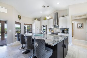 A modern kitchen with a central island, bar stools, and a view to the outdoors. - Hidden Gem in Cape Coral with heated pool and spa, on wide canal 3b/2b (Cape Coral)