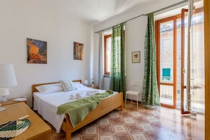 A hotel room with a bed, a desk, a chair, a window with curtains, and artwork on the walls. - Casa La Conchiglia - Casa la Conchiglia (Porto Recanati)