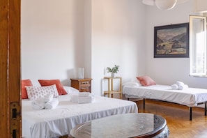 Quarto de hotel com duas camas, uma mesa pequena, um quadro na parede e uma janela.