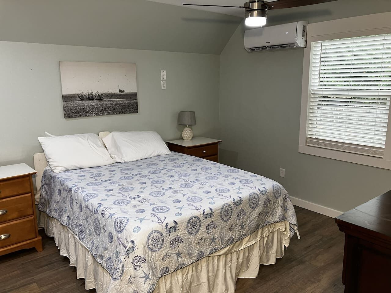 A bedroom with a bed, nightstands, a lamp, a ceiling fan, and a window with blinds.