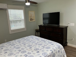 A bedroom with a bed, dresser, television, and window with blinds.