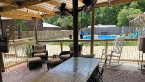 Ein überdachter Patio-Bereich mit einem langen Tisch, Stühlen und einem Pool im Hintergrund.