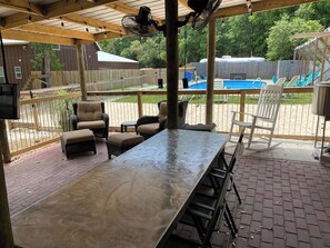 Un patio techado con una mesa larga, sillas y una piscina al fondo.
