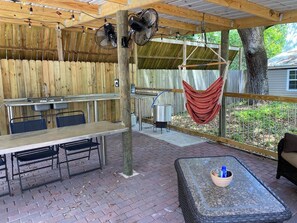 Un patio exterior con mesa y sillas de madera, una hamaca colgante y suelo de ladrillo.
