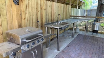 An outdoor kitchen area with a grill, sink, and gas stove.