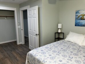Un dormitorio con una cama, una mesita de noche, una lámpara y una puerta que da a otra habitación.