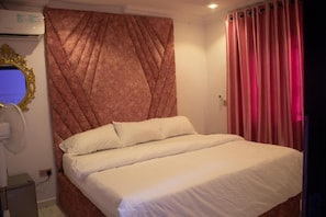 Una camera d'albergo con un letto, un condizionatore d'aria a parete, uno specchio con cornice dorata e una finestra con tende.