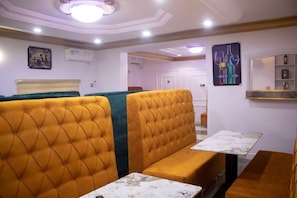 Una camera d'hotel con area salotto caratterizzata da divanetti imbottiti gialli e verdi, un tavolo con piano in marmo e una mensola a parete con oggetti decorativi.