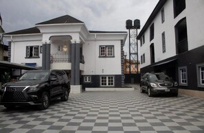 Un edificio de dos pisos con fachada blanca y techo negro, que cuenta con un camino de entrada a cuadros y automóviles estacionados.