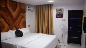 Una habitación de hotel con cama, ventilador de pie, puerta y aire acondicionado instalado en la pared.