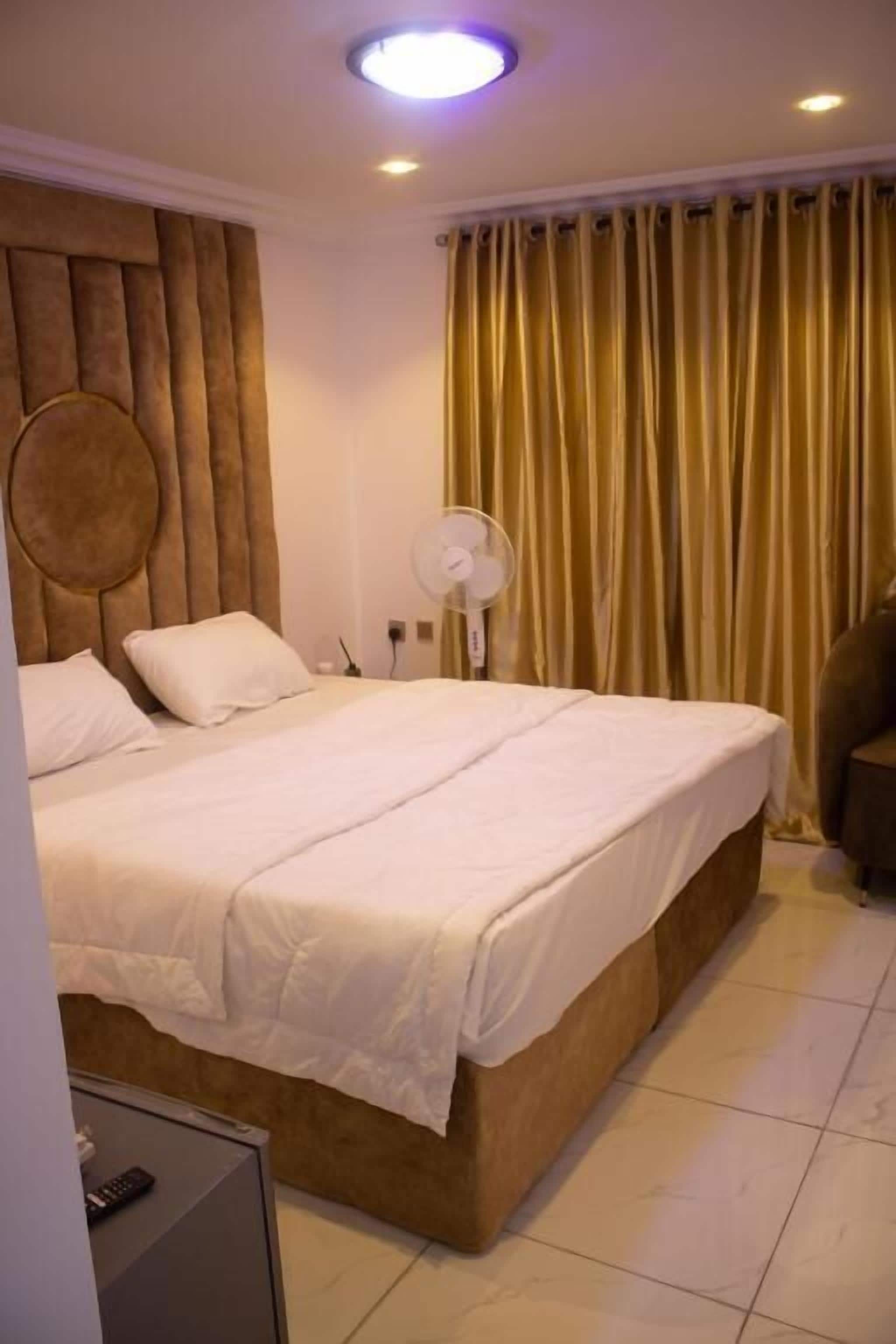 Une chambre d’hôtel avec un grand lit, une table de chevet, un ventilateur et un rideau.