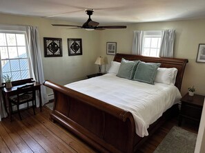 Ein Schlafzimmer mit einem großen Bett, einem Schreibtisch, einem Sessel, einem Deckenventilator und gerahmten Kunstwerken an den Wänden.
