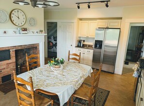 A dining area with a table set for four, a fireplace, and a kitchen with modern appliances. - The 1860 Farmhouse: A Peaceful New England Retreat (Barrington)