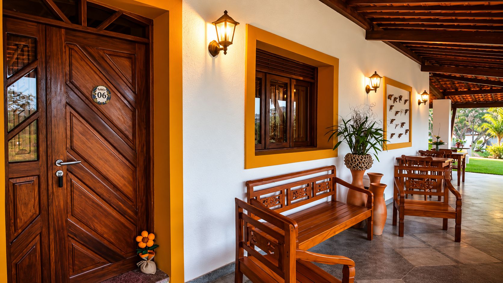 Una puerta de madera con una placa de número, un banco, una mesa, sillas y luces fijadas a la pared.